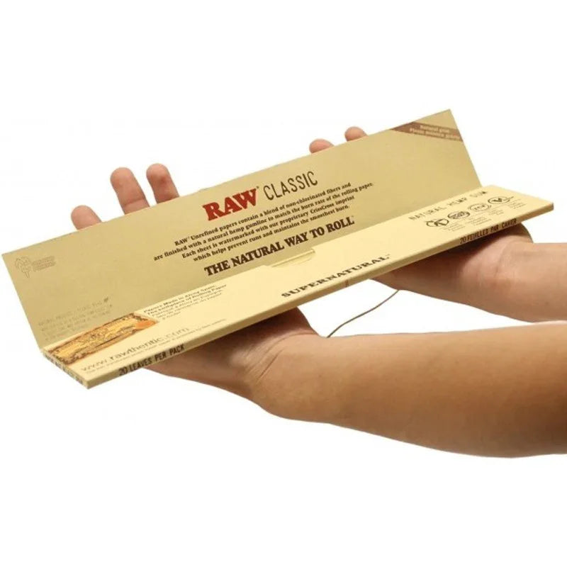 Papel para fumar RAW Classic tamaño gigante sostenido con ambas manos, ideal para armar cigarrillos.